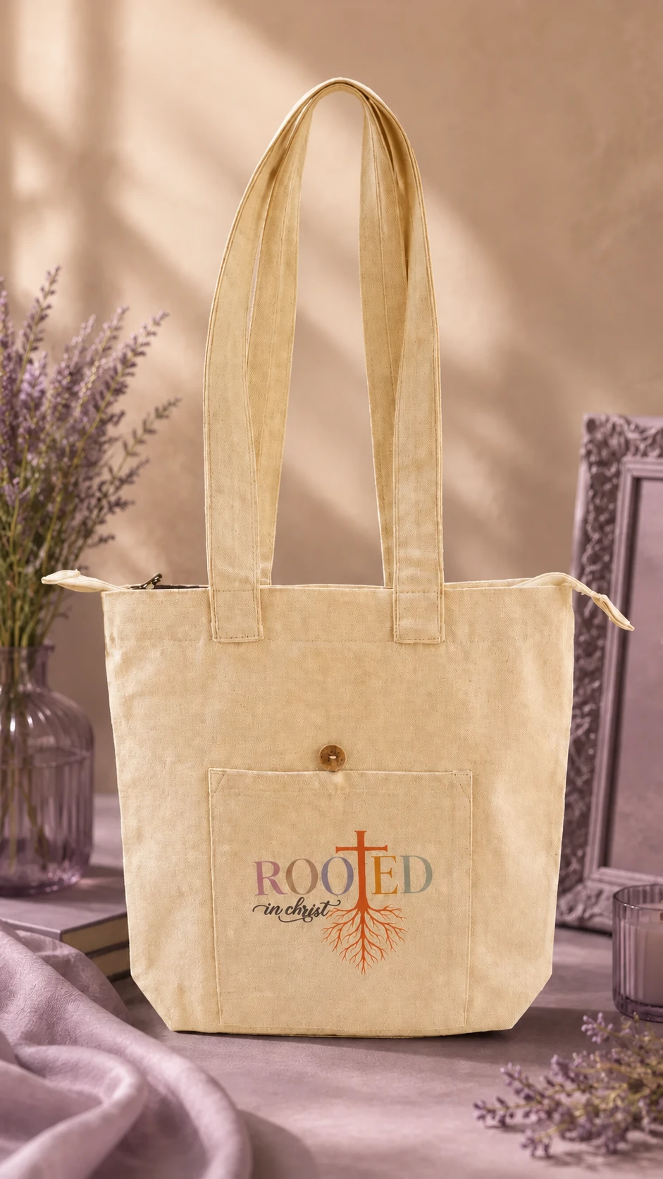 Cream Rooted in Christ Premium Tote standing upright, front pocket printed with a cross and roots.